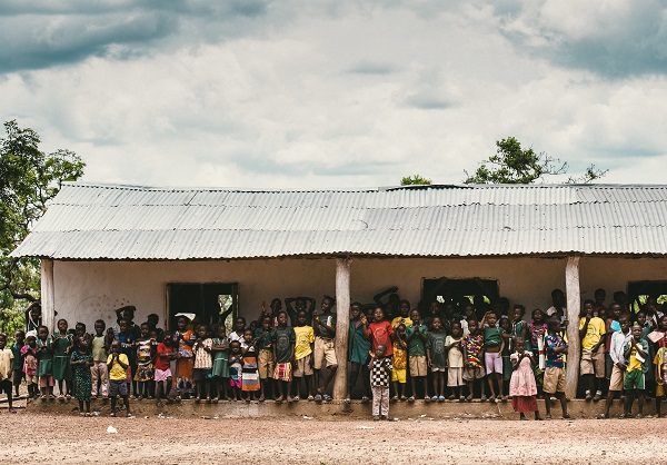 30 odd kids standing outside a school, waving at the camera