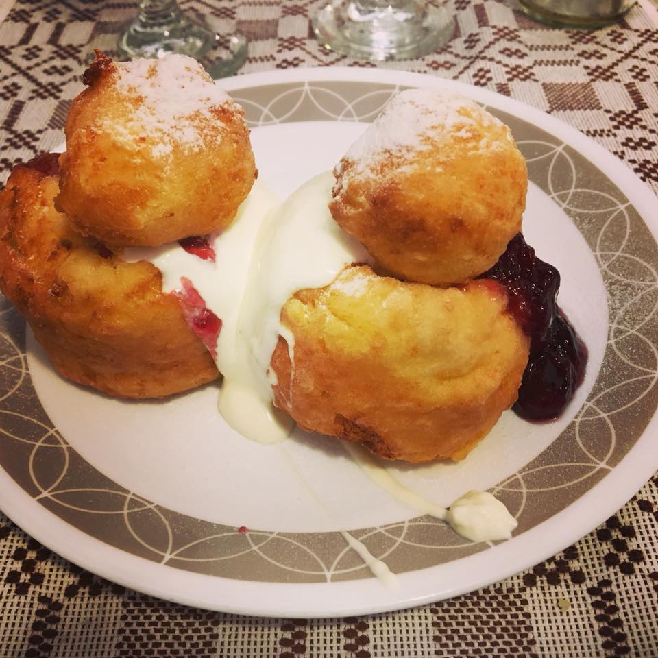 Photo of two papanasi topped with sour cream and strawberry jam