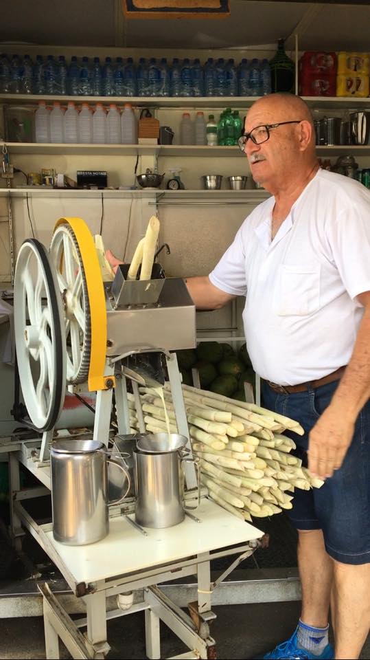 Photo of a man pushing sugar cane through a machine which squeezes out the juice. 