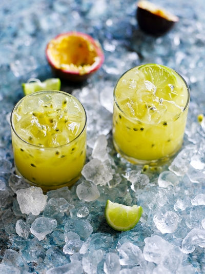 Two passion fruit caipirinhas with a "dig out" passion fruit in the back ground and a squeezed lemon in the foreground. 