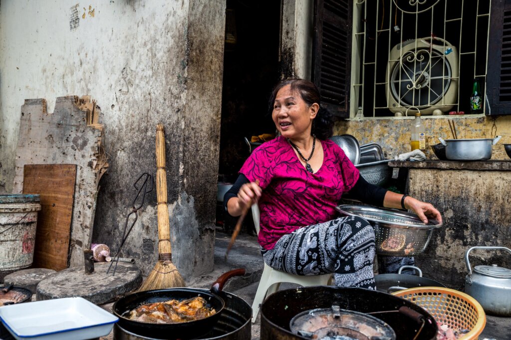 One of the top things to do in the Hanoi Old Quarter is watch life go by, in this case, a lady cooking on the pavement outside her house