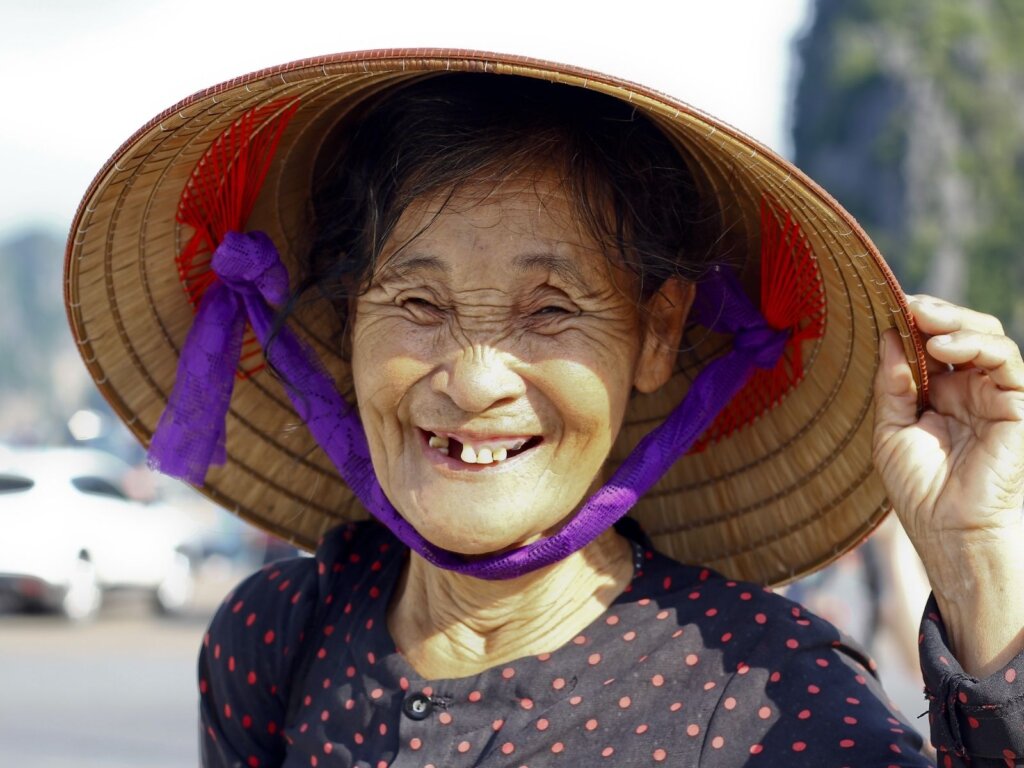 Smiling chinese lady with large toothless gaps and deep wrinkles, wearing a bamboo woven hat. 