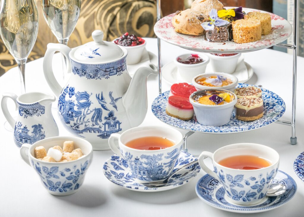 Afternoon tea, with porcelain mugs, saucers and tea pot, as well as yummy looking bite sized cakes