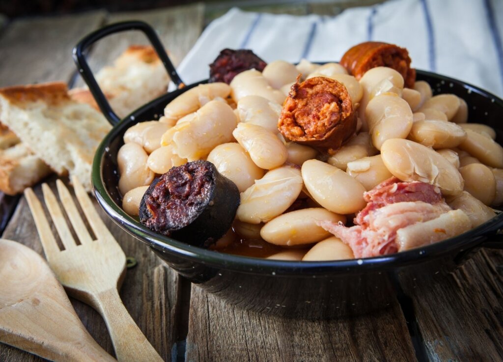 A photo of a big plate of beans with chorizo and black pudding, a typical of Asturias Eating local produce is the best way not only to remain on budget but also to guarantee you are eating the best that locality has to offer in Spain. 