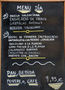 Photo of a menu del dia which is one of the best ways to eat in Spain as a budget. 
1) paella valenciana
ensalada de arroz
gazpacho andaluz
hervido valenciano
2) Bistec de ternera encebollado
Hamburguesa con patatas y ensalada
Bacalado a la plancha
Lomo fresco a la plancha
Calamares romana 
Croquetas de bacalao
Huevos con bacon
Pan, bebida, postre o cafe €9,95