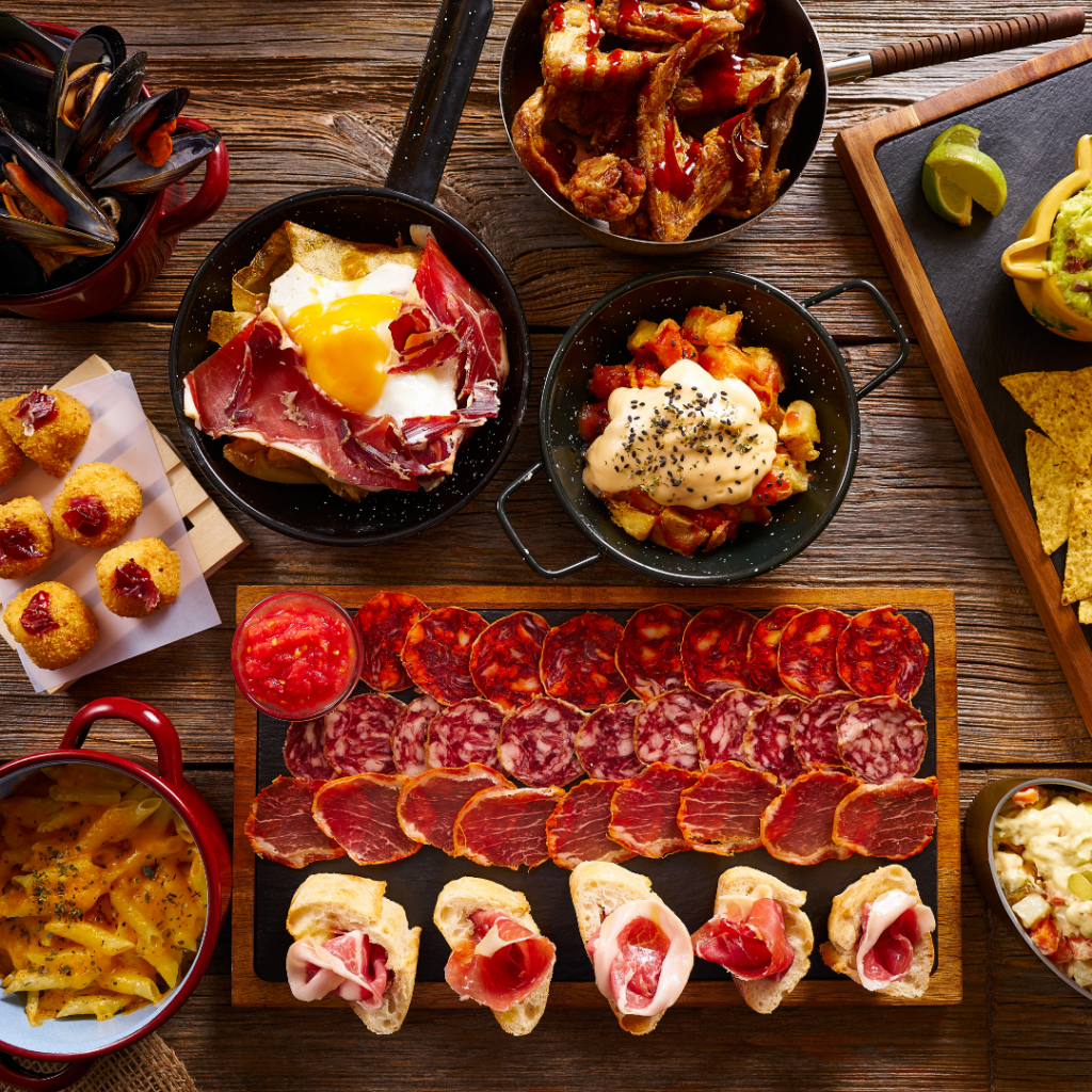 A highlight of any Spanish trip is the food, and this photo shows a table full of delicious different Spanish dishes including pasta, patatas bravas, croquetas, an assortment of meat and a few others that I don't recognise. 