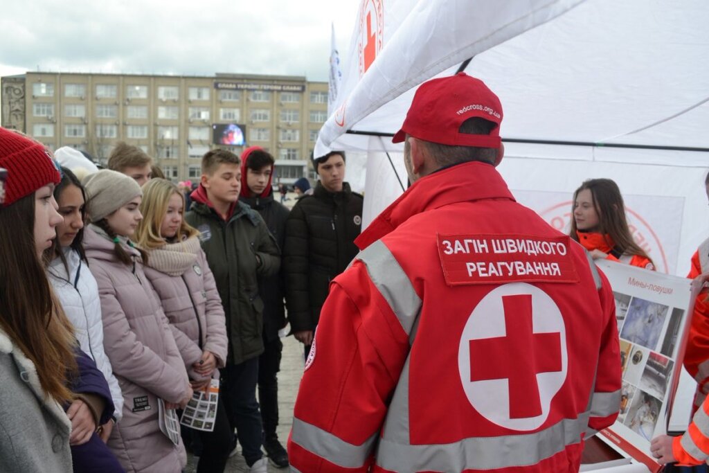 Photo of a man wearing a red cross jacket speaking to a group of teenagers