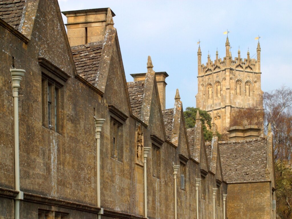 A row of old fashioned homes with the Chipping Campden church tower peaking up above them. 