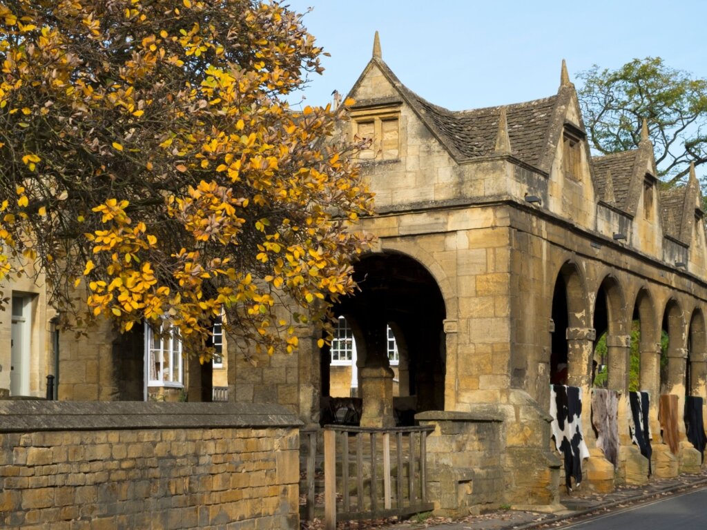 Chipping Campden Market Hall with cow hides hanging on the side and an autumnal tree in front