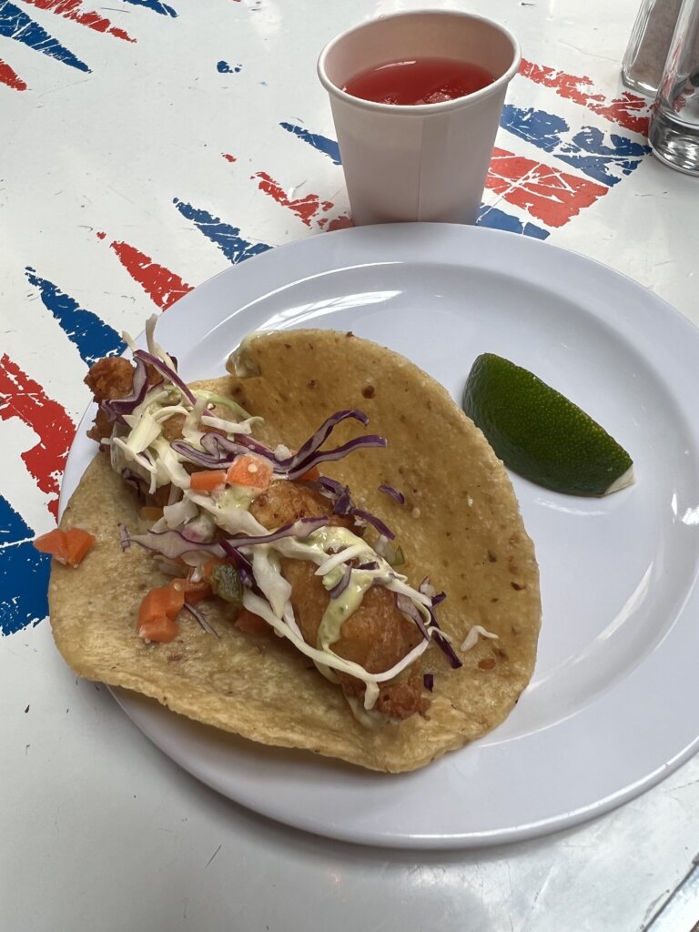 A delicious fish taco with a wedge of lime and a glass of watermelon