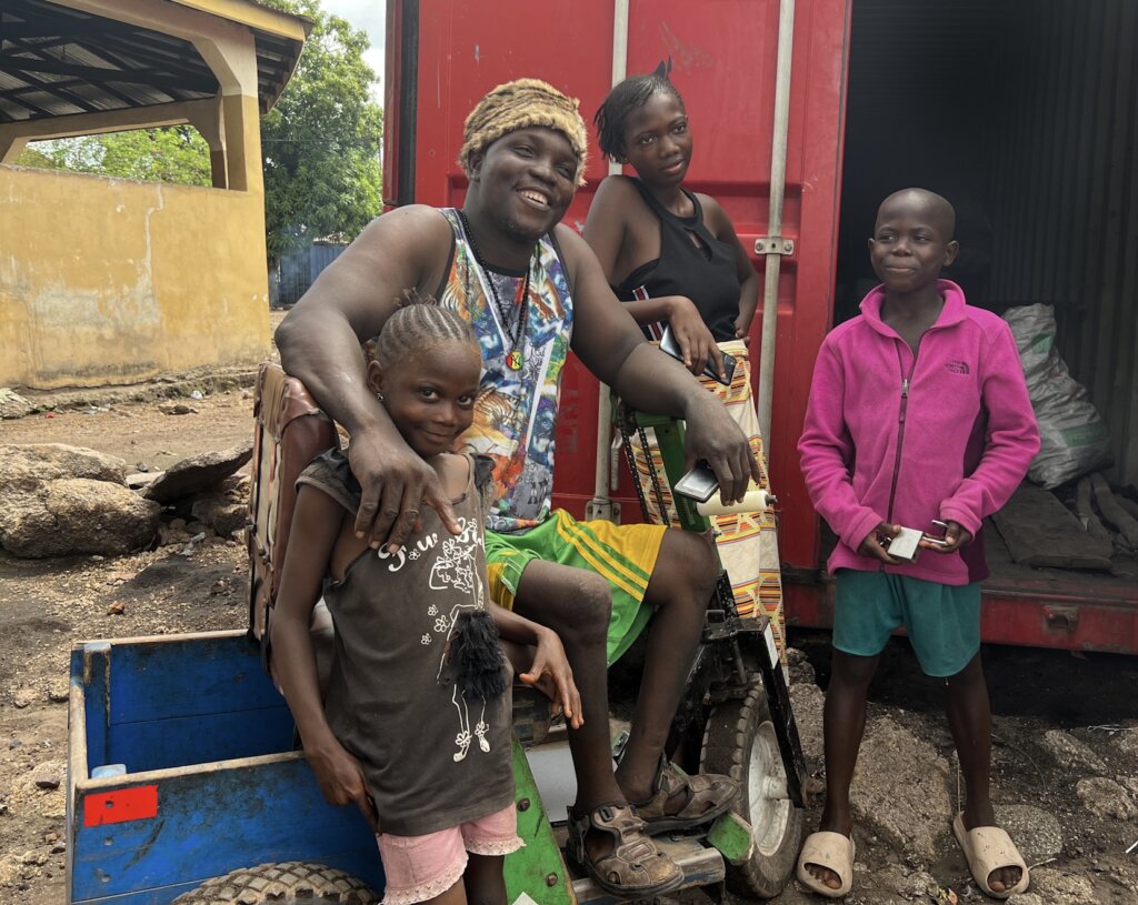 A polio survivor sitting on his mobility scooter (manual) standing next to his three kids. 