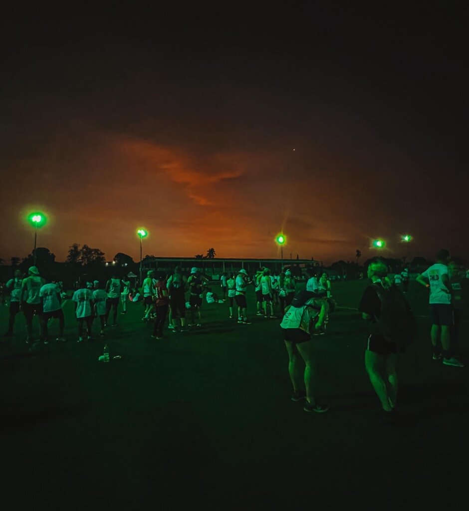 A dark photo of the brightening sky with Sierra Leone marathon runners stretching in the background ready to get going