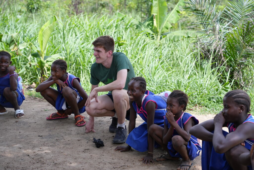 One of the marathon runners sits with kids at school. They are all smiling, potentially even playing a game!