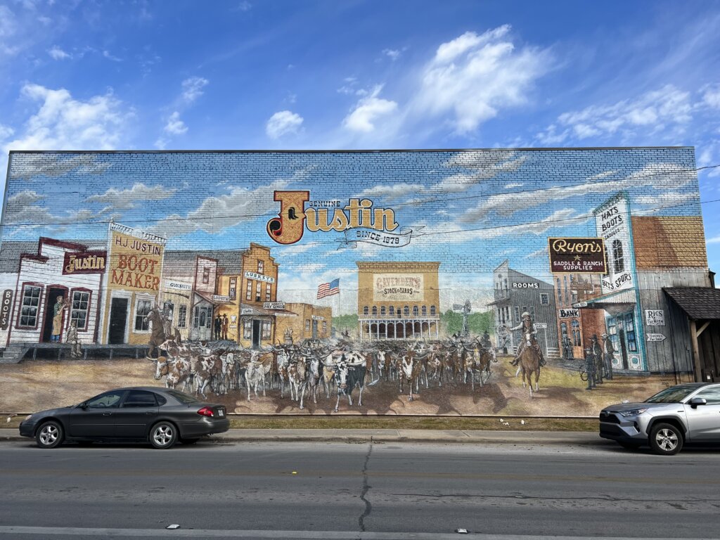 A beautiful mural of an old town centre with a herd of cattle moving through it