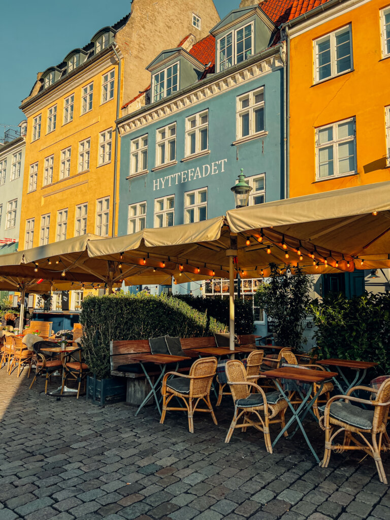 A cafe with warm fairy lights provides the foreground for a row of colourful townhouses. Wandering Nyhvn is a great way to explore the city for free