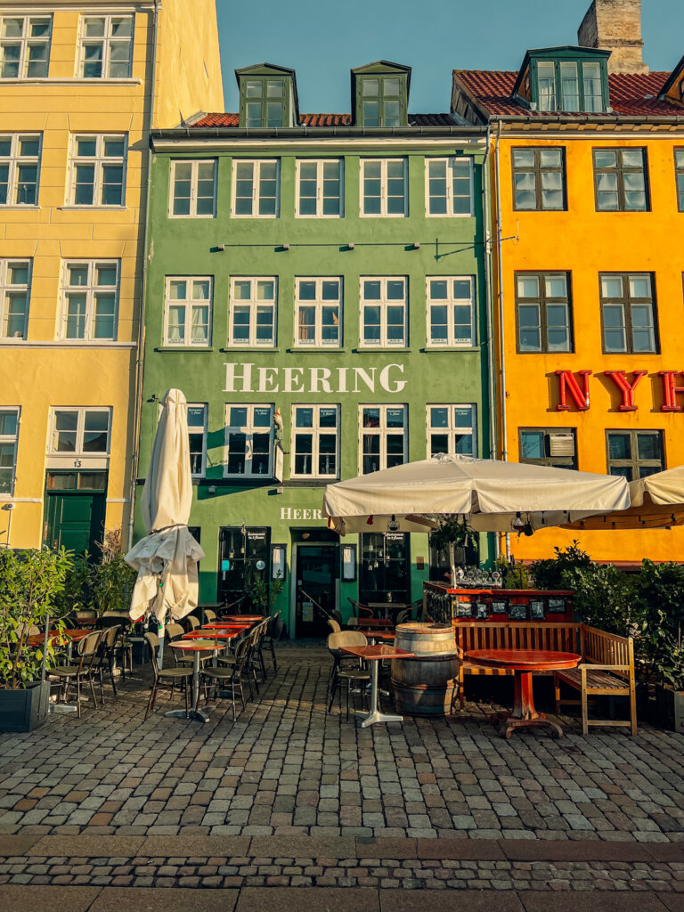 One of the many colourful buildings in Nyhavn. A green building with lots of windows flanked by two yellow building, all with lots of windows. A walk through Nyhvn is one of the best free things you can do in Copenhagen