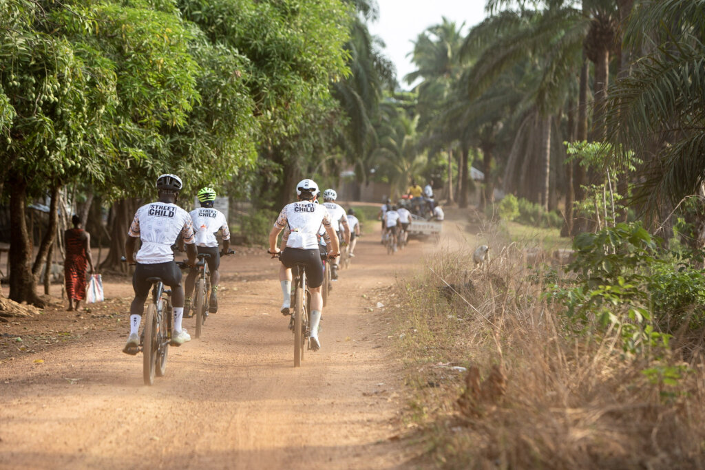 The group of cyclist pedalling down one of the red dirt roads flanked by palm trees