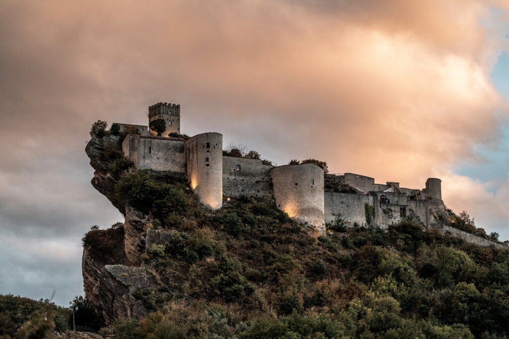 A castle precariously balanced on the rock, high on the mountains sky with a cloudy sky above it. One of Italy's off the beaten path hidden gems