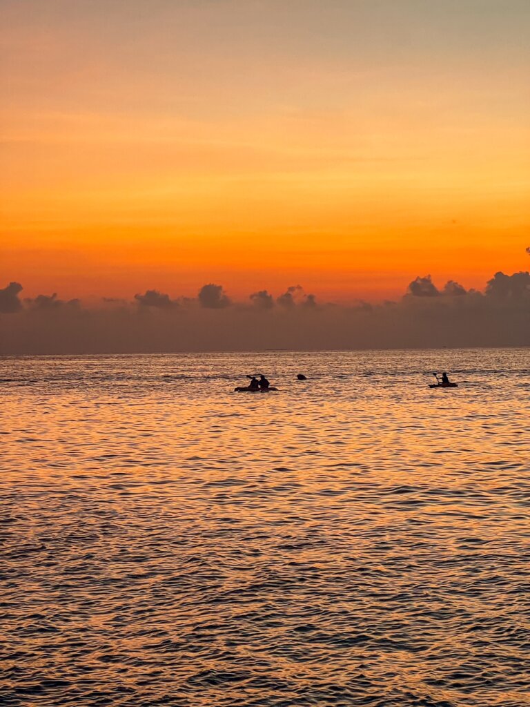 The sky lit up in different shades of orange with some kayakers in the horizon