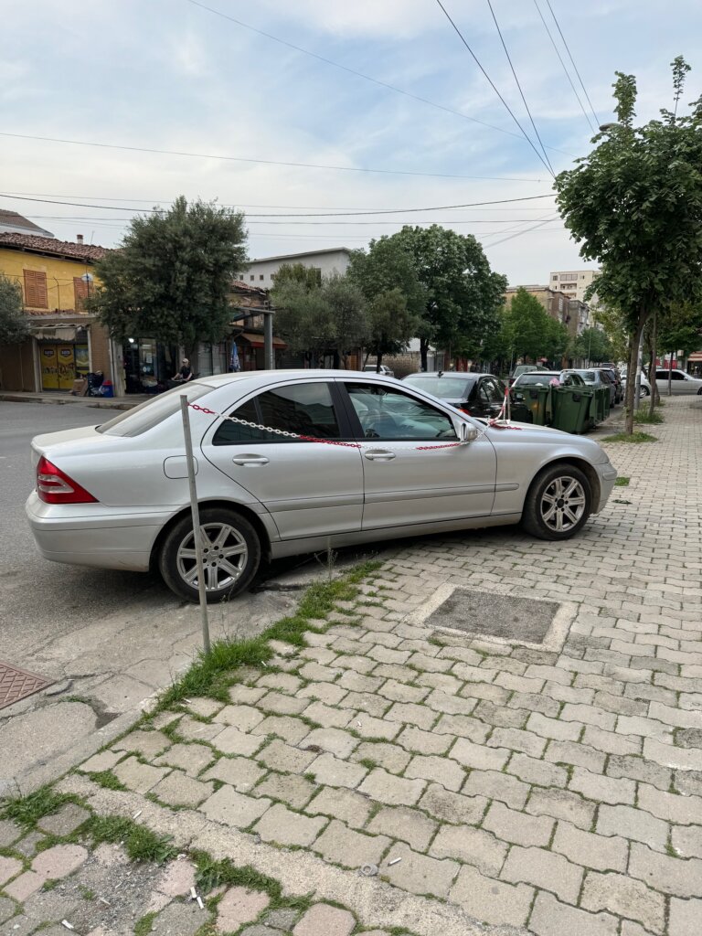 An example of Albanian parking. A car parked half on the pavement and with a chain over its bonnet