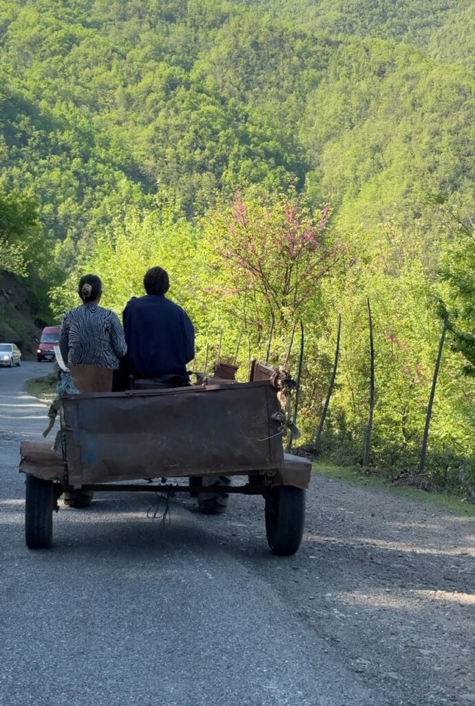 A couple riding on an old tractor down one of the Albanian roads