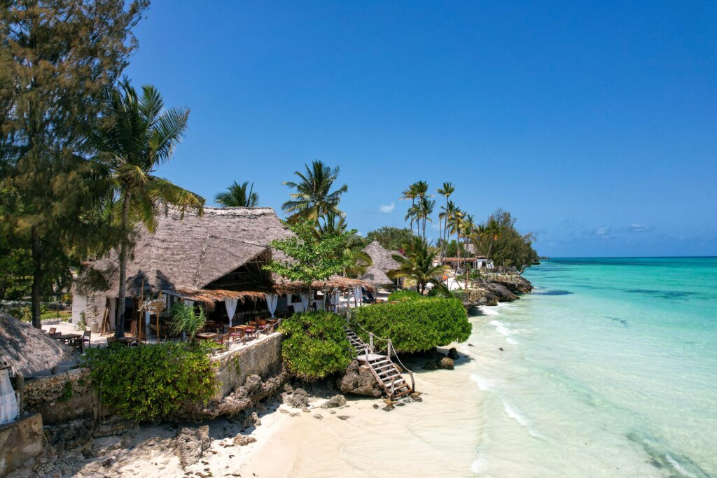 A restaurant perched on the coast of Zanzibar, white sand beach below and turquoise waves gently crashing in