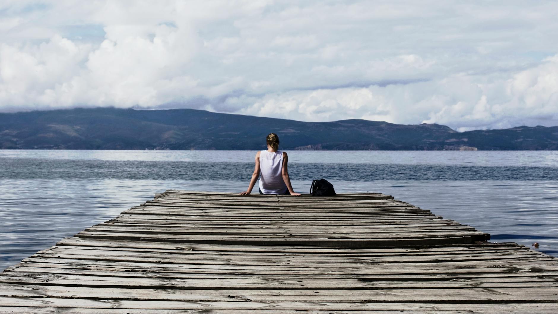 person sitting on brown wooden dock under cloudy blue sky